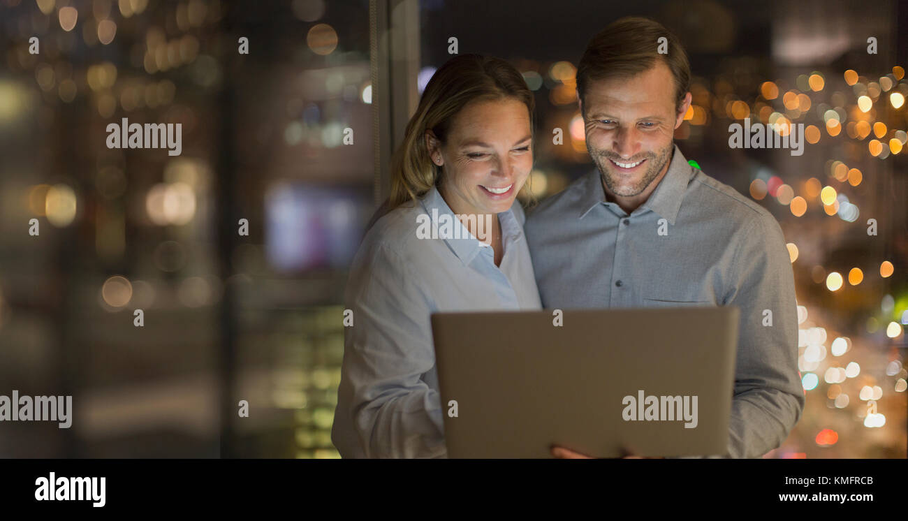 Lächelnder Geschäftsmann und Geschäftsfrau, die spät am Laptop im Büro arbeitet Nachts Stockfoto