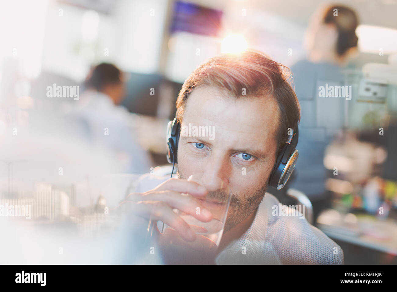 Geschäftsmann mit Kopfhörern Trinkwasser im Büro Stockfoto