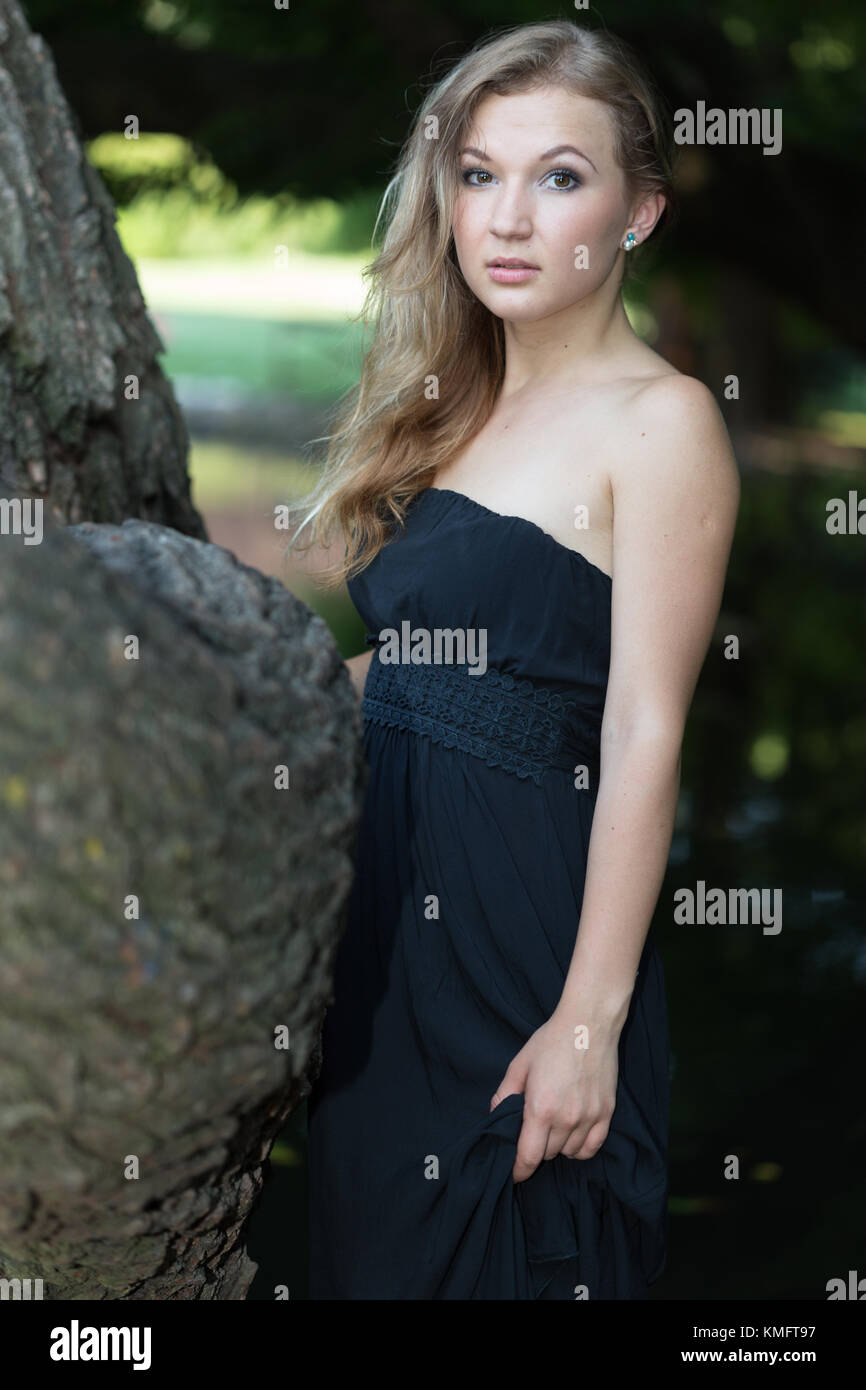 Schöne junge Frau im Ballkleid am Baum Stockfoto