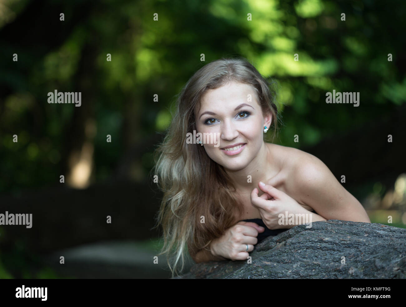 Schöne junge Frau im Ballkleid am Baum und lächelnd Stockfoto