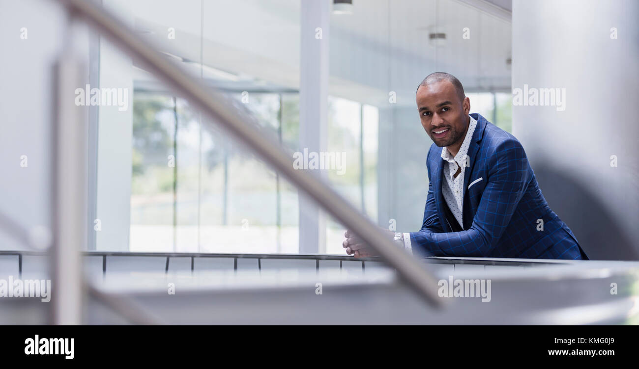 Portrait lächelnder Geschäftsmann, der sich im Büro auf Geländer stützt Stockfoto