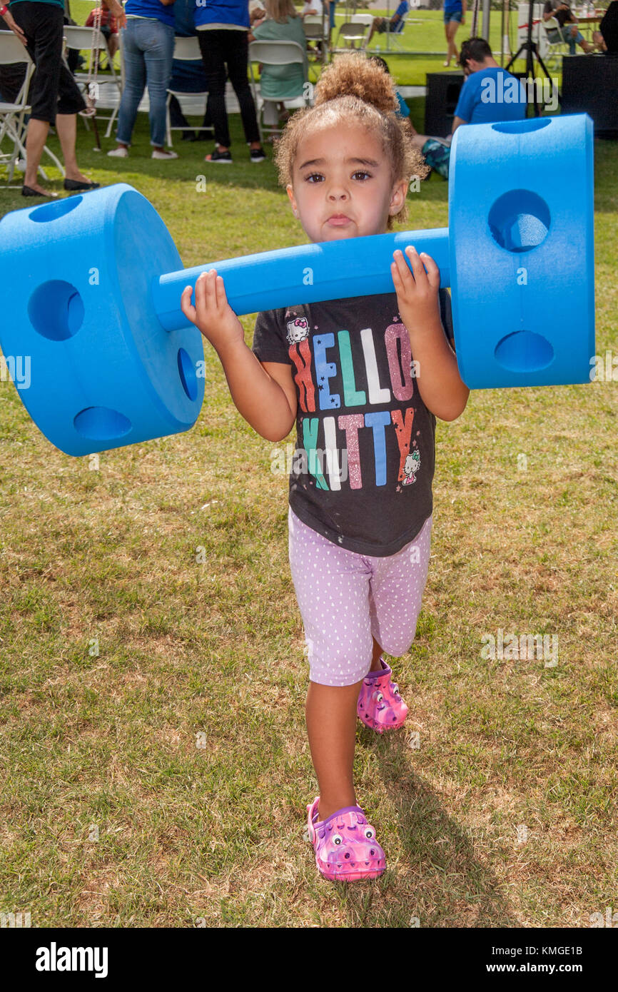 A 2-year-old African American Girl leicht Hefts ein Barbell aus Schaumgummi an einer Messe in Fountain Valley, CA. Stockfoto