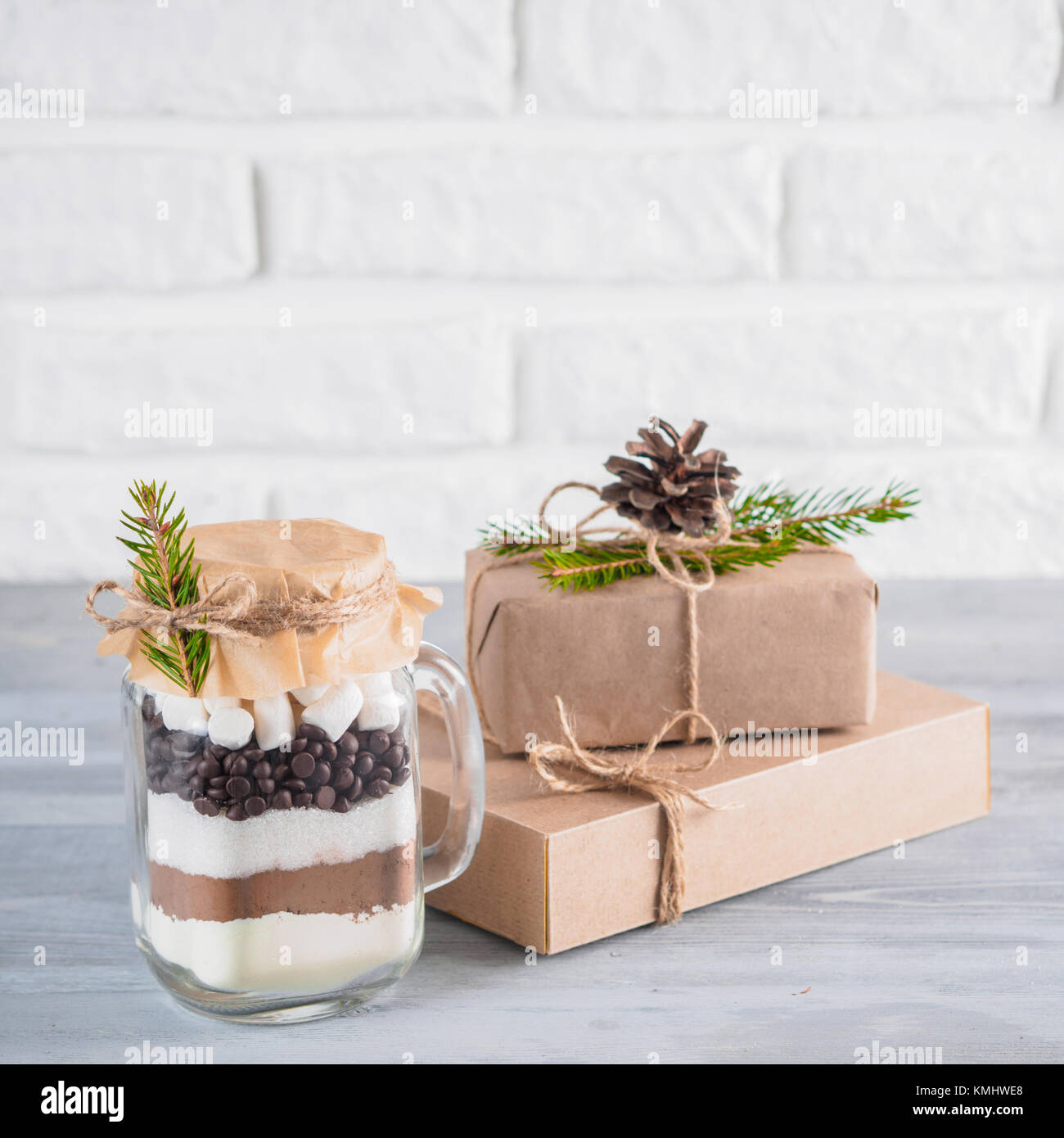 Heiße Schokolade Mix im Marmeladenglas und rustikalen Geschenkboxen auf grau Tabelle und weiße Wand. Weihnachten und Winter Urlaub budget-freundliche Geschenke Idee. Kopieren Stockfoto