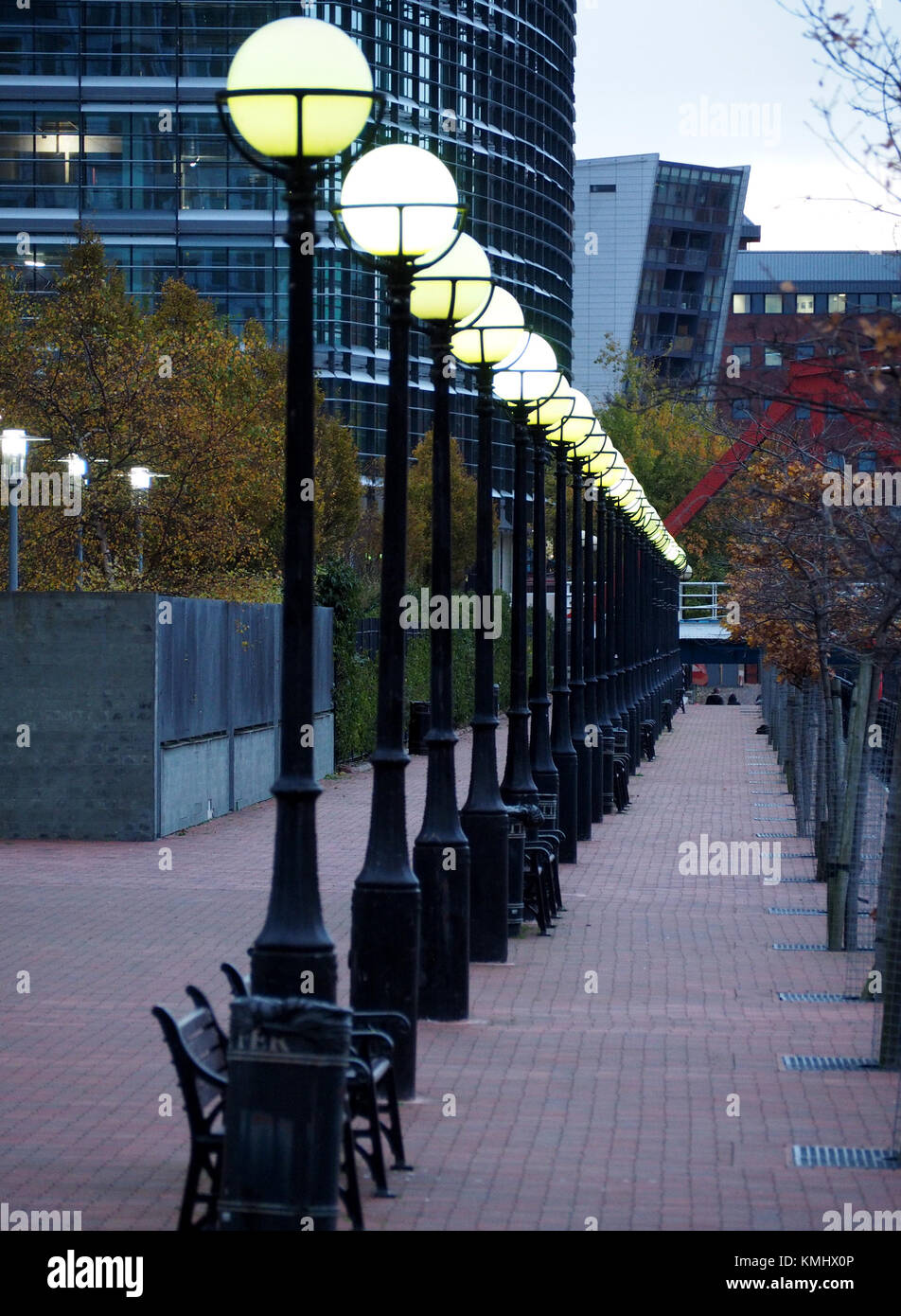 Einen zurückweichenden Linie der Globus Straßenlaternen hell in der Dämmerung scheint auf der Fußgängerzone Kai in Salford Quays, Salford, Manchester, UK Stockfoto