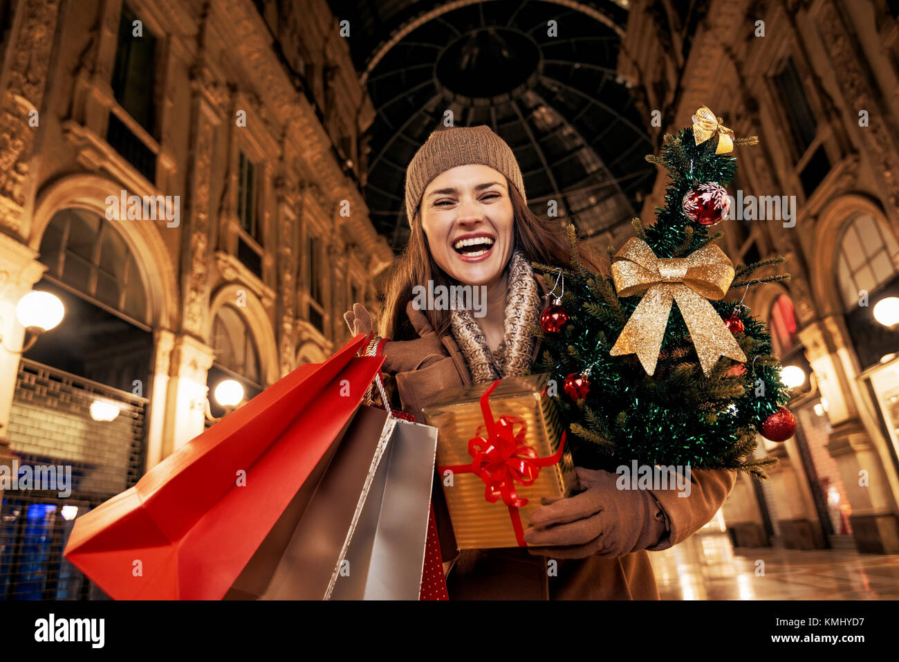 Auf einem riesigen Weihnachtsgeschäft in der italienischen Modehauptstadt. Portrait von fröhlichen elegante Frau mit Weihnachtsbaum und Einkaufstaschen in der Galleria Vittorio Em Stockfoto
