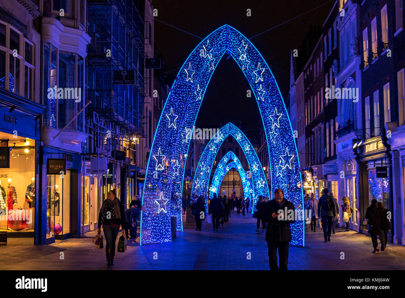 Menschen, die zur Weihnachtszeit an der South Moulton St entlang gehen, die mit großen blauen Weihnachtsbögen geschmückt ist, London, Großbritannien Stockfoto