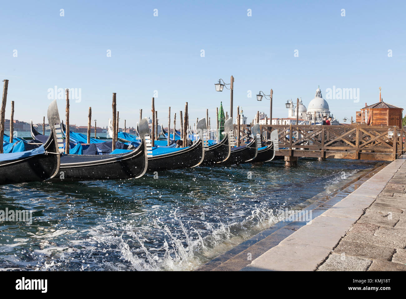 Gondeln an San Marco Reiten hoch im Wasser auf einem Acqua Alta Tide mit Splash und Blick auf Baslica di Santa Maria della Salaute, Venedig, Italien Stockfoto
