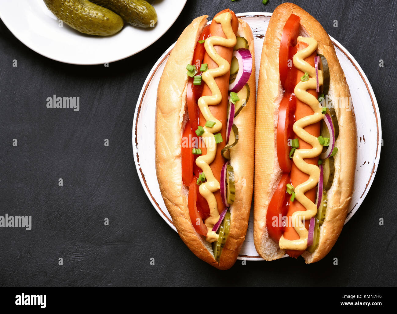 Fast food. Hot dogs mit Tomaten, Gurken, Zwiebel mariniert auf dunklem Hintergrund. Ansicht von oben, flach Stockfoto