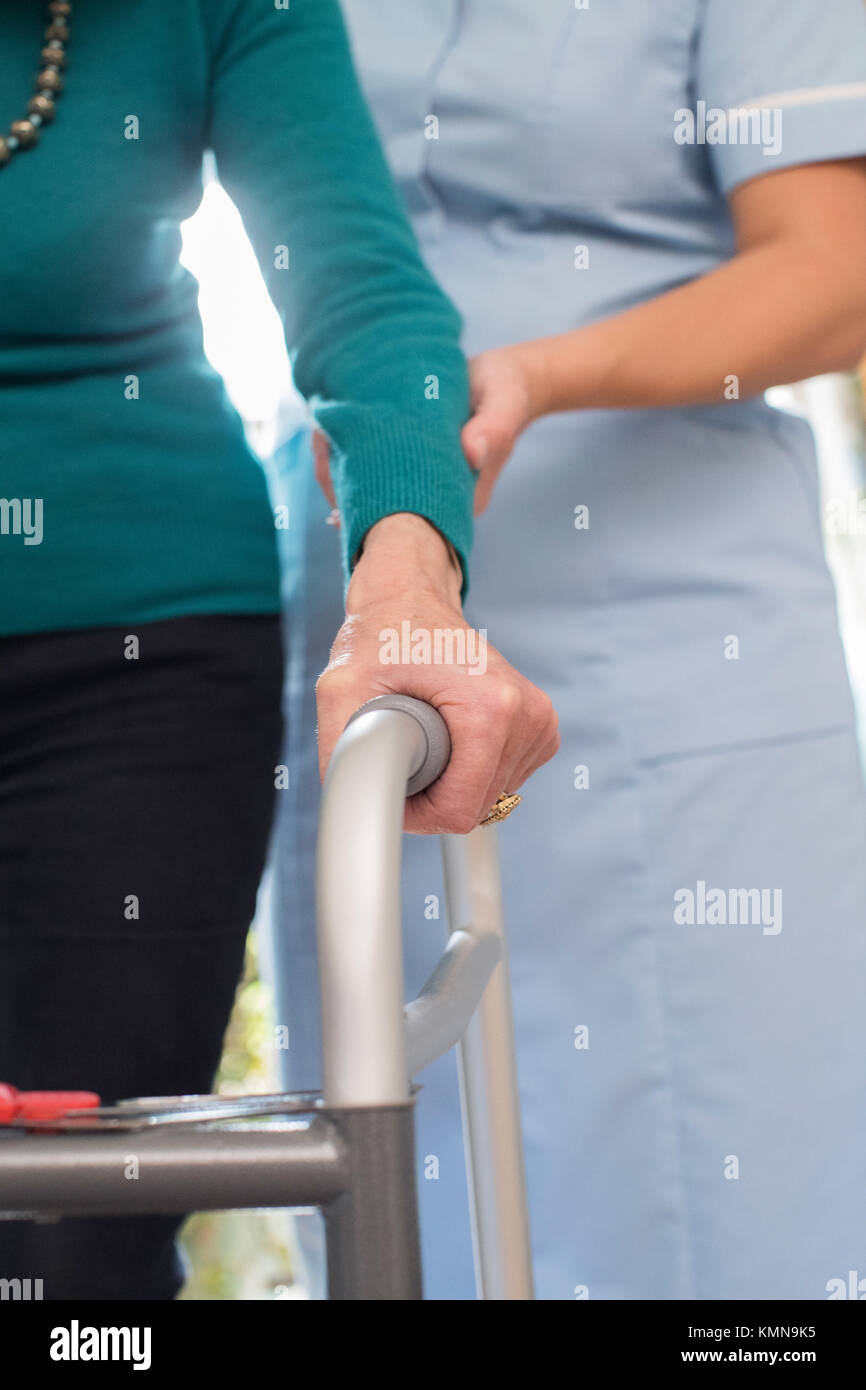 Die ältere Frau Hände auf Gehhilfe mit Sorgfalt Arbeiter im Hintergrund Stockfoto