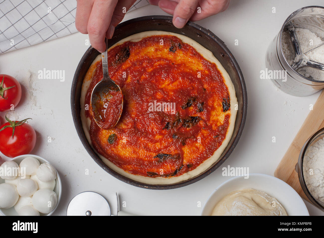 Nahaufnahme der Hand des Chefkochs hinzufügen Tomatensoße auf der Pizza Teig. Stockfoto