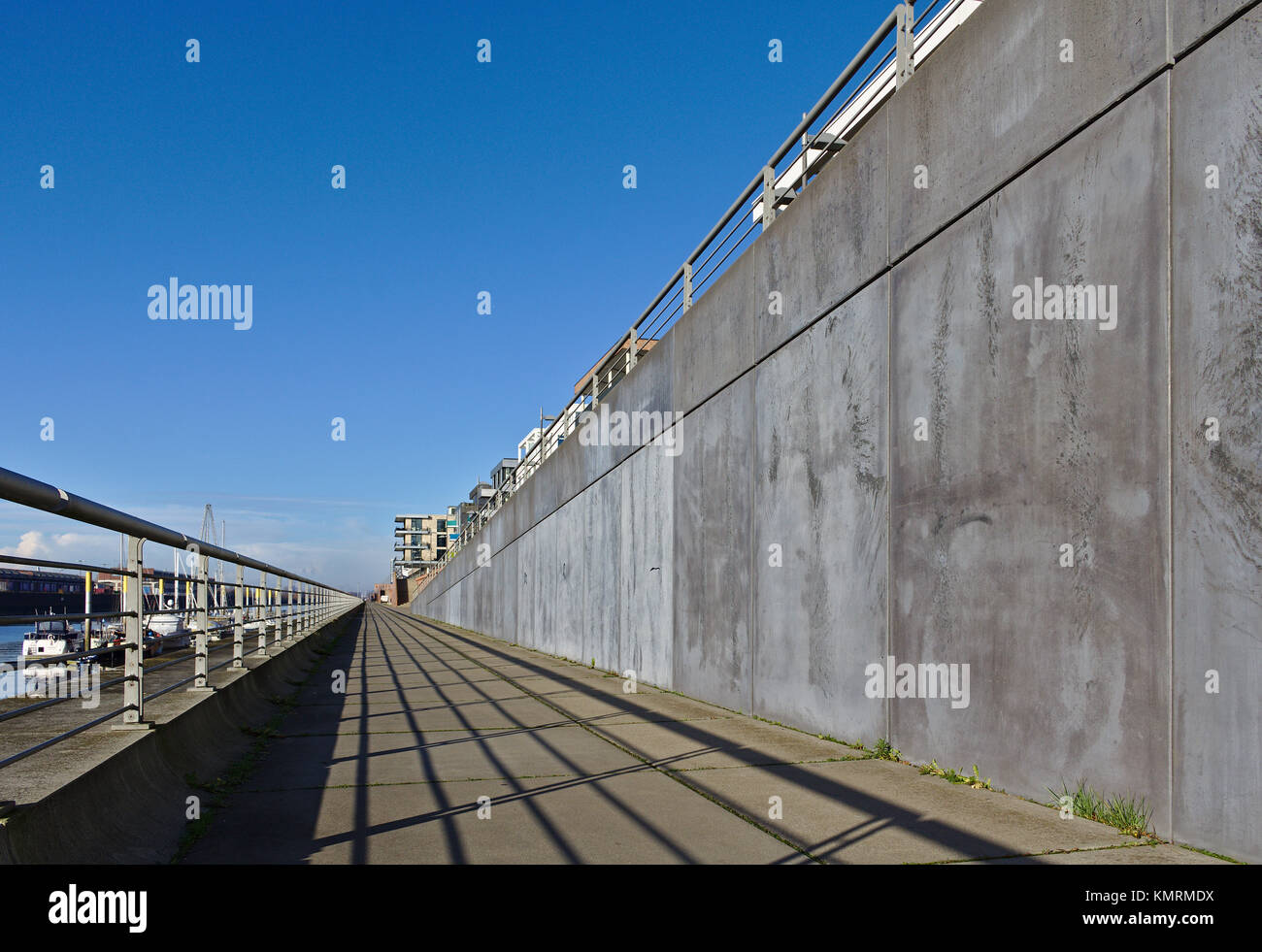 Esplanade entlang der Europa Hafen in Bremen, Deutschland mit Metall Geländer, graue Betonwand, angelegte Segelyachten und ein strahlend blauer Himmel Stockfoto