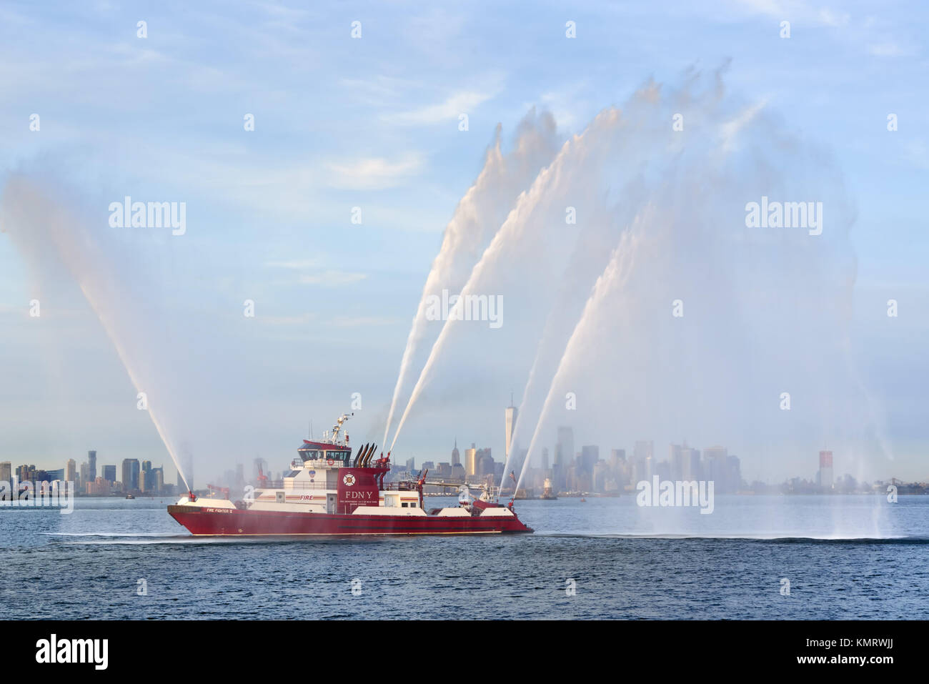Fire Fighter II Feuerlöschboot mit Wasserstrahlen bei voller Leistung vor der Lower Manhattan (einschließlich das One World Trade Center) bei Sonnenuntergang. New York City Hafen Stockfoto