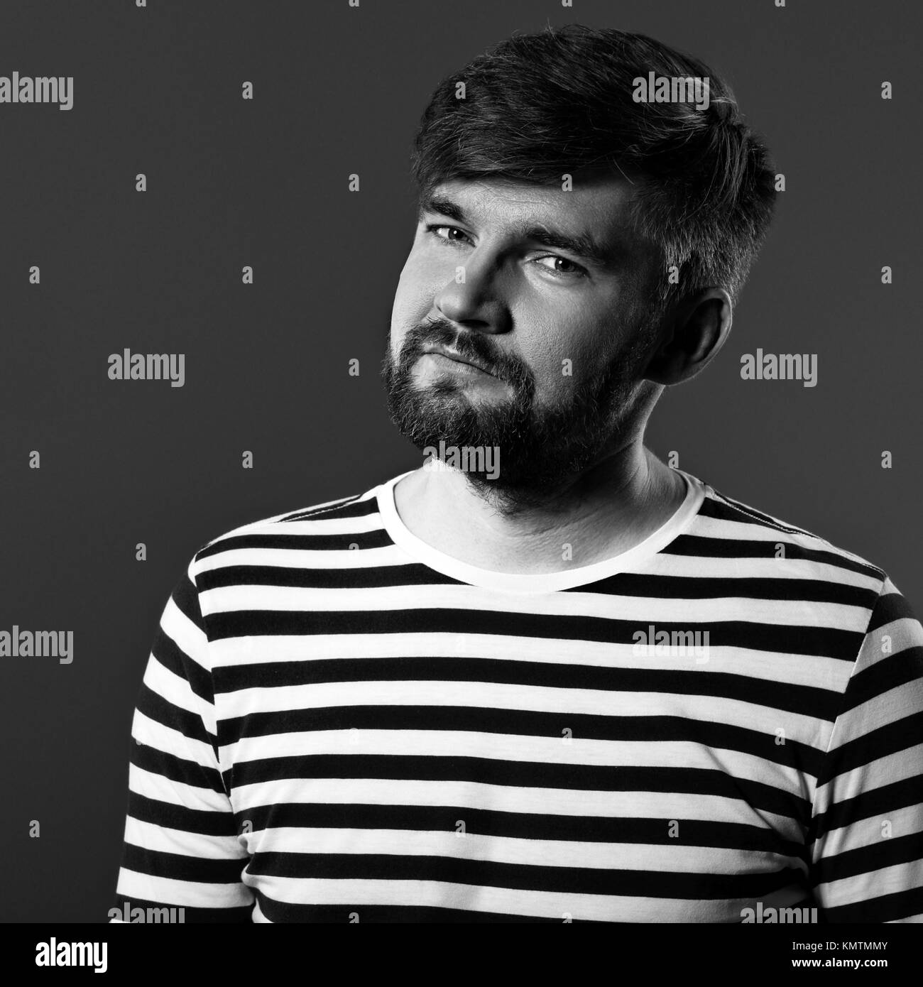 Bärtige lächelnde Mensch in lässig-gestreiftes T-Shirt auf grauem Hintergrund mit der leere Raum. Closeup Portrait. Schwarz und Weiß Stockfoto