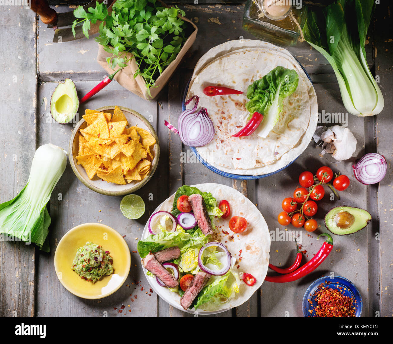 Draufsicht auf mexikanischen Stil Abendessen mit Gemüse, Tacos, Nachos Chips und Guakomole, serviert auf grauem Holztisch. Stockfoto