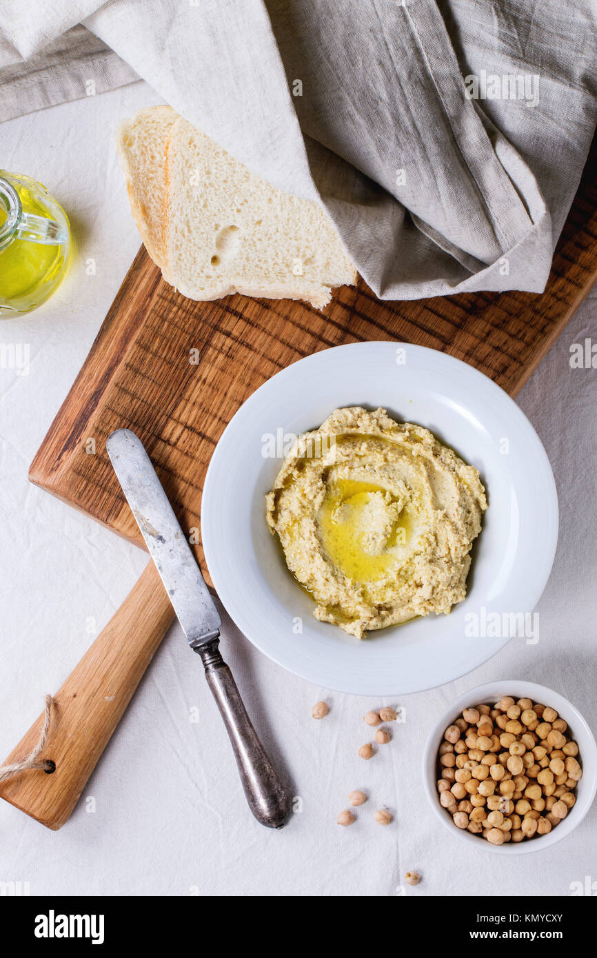 Teller mit hausgemachten Hummus mit Brot, Olivenöl und rohe Küken - Erbse, auf Holz Schneidebrett über rustikale Tisch serviert mit grau Tischdecke. Ansicht von oben Stockfoto