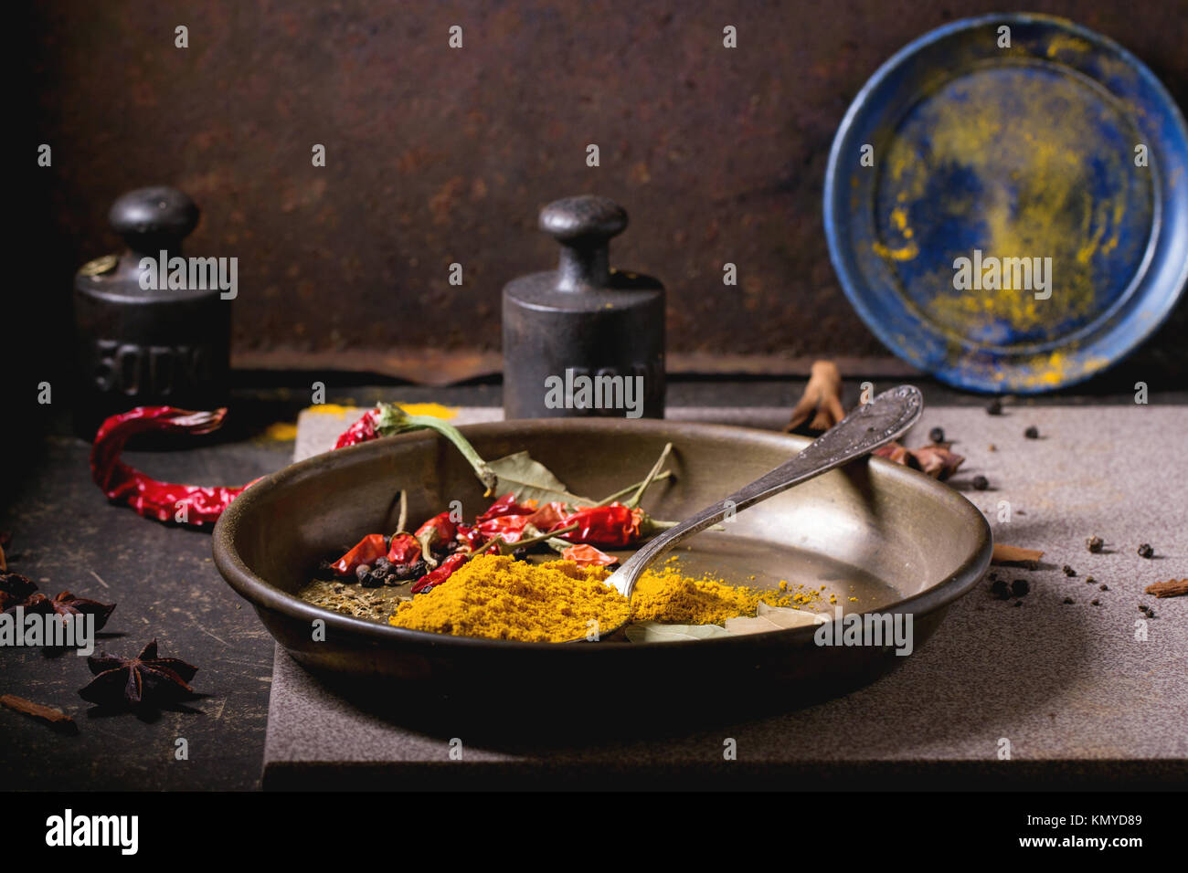 Gewürzen Kurkuma und trockenen Reh hot Chili Peppers auf Metallplatte, Srved über dunklen Tisch mit Vintage Gewicht und blaue Keramik-Platte. Stockfoto