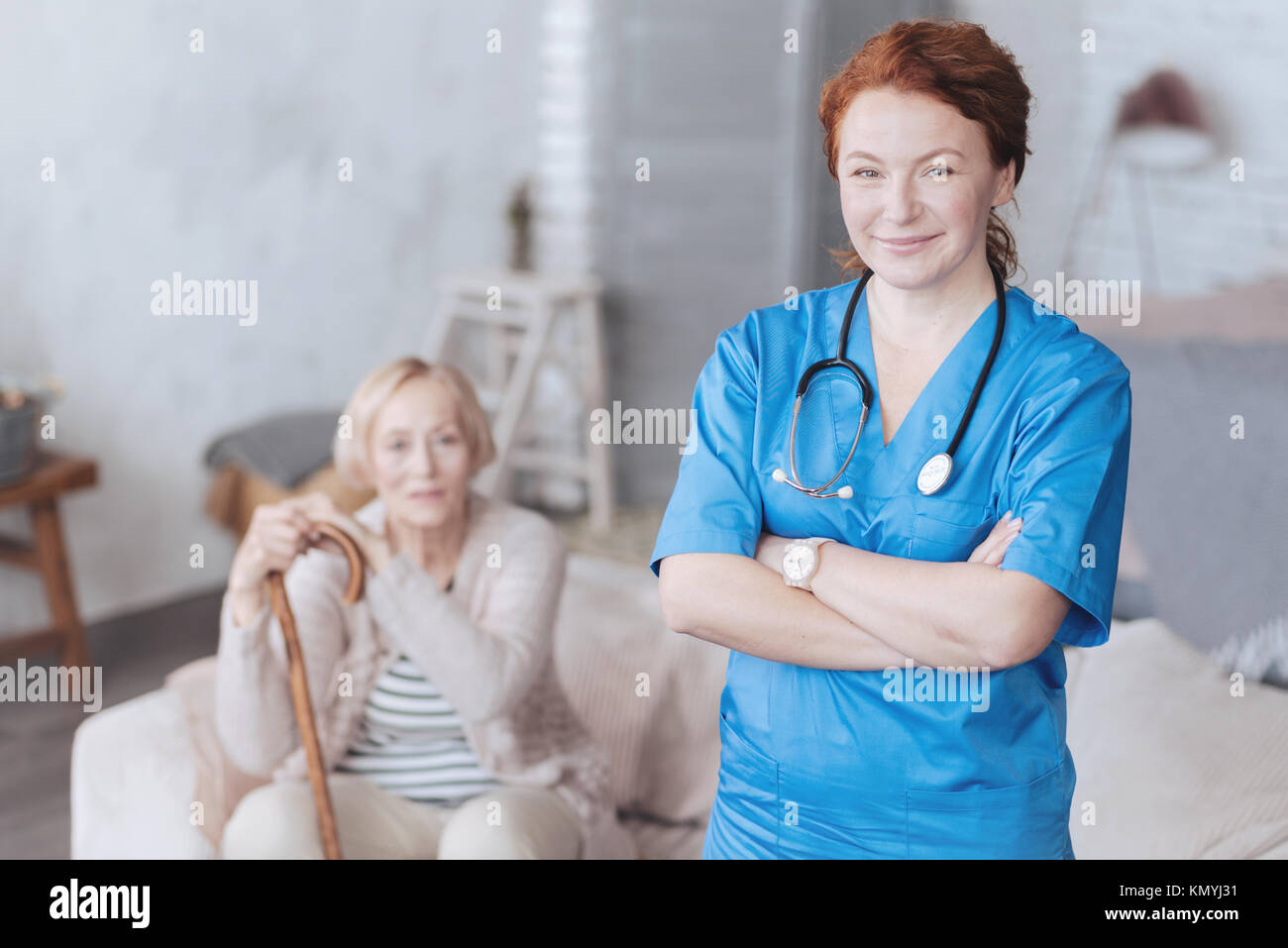 Fröhliche reife Krankenschwester mit Waffen posiert gekreuzt Stockfoto