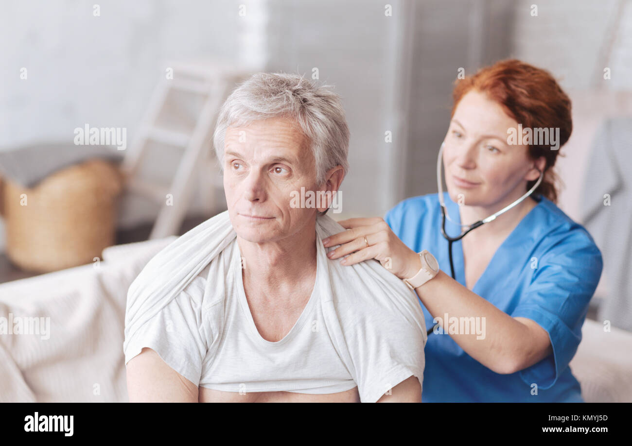 Fröhliche Krankenschwester mit Stethoskop Abhören der Lunge klingt der Patienten Stockfoto