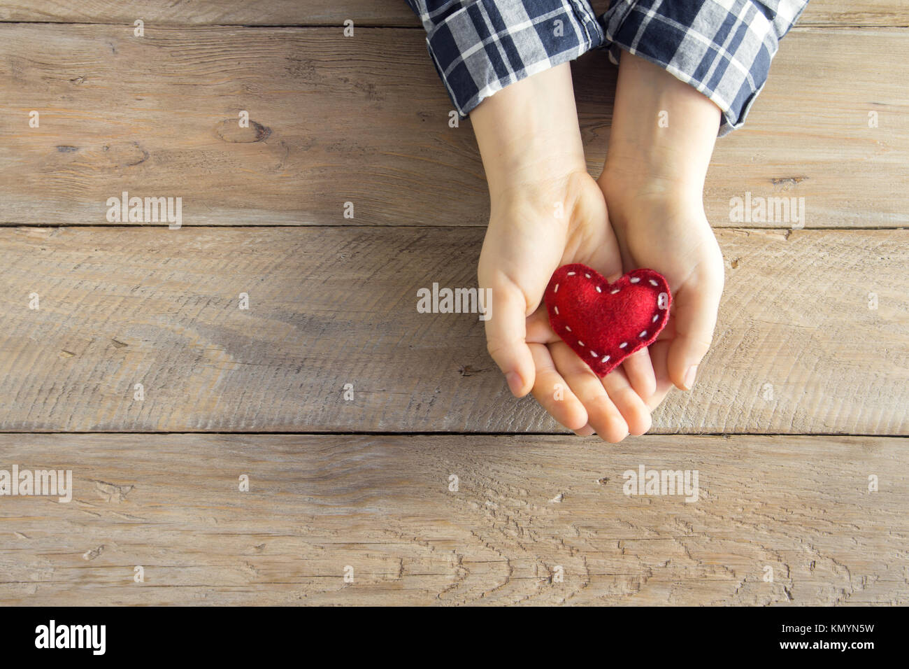 Rotes Herz in Kind Hände über Holz- Hintergrund, kopieren. Güte, Liebe und Nächstenliebe Konzept, hand made Valentinstag Geschenk. Stockfoto