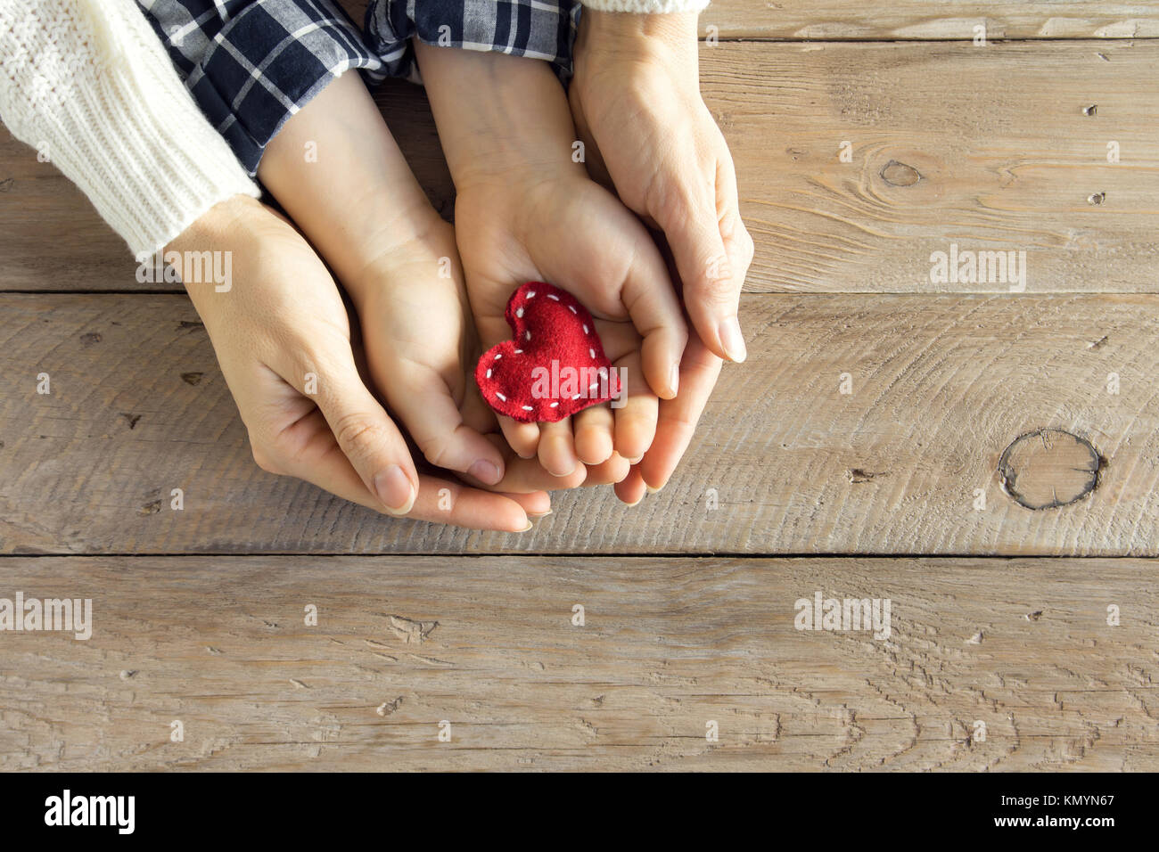 Rotes Herz im Kind und weibliche Hände über Holz- Hintergrund, kopieren. Freundlichkeit, Familie, Liebe und Nächstenliebe Konzept, zum Valentinstag oder Muttertag da Stockfoto