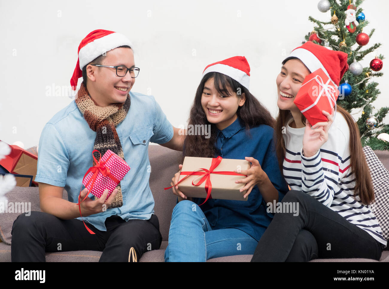 Gruppe von Asien Freunde sitzen auf einem Sofa feiern Weihnachten und Silvester Party mit Geschenk Austausch auf schmücken Baum, Geschenke urlaub Konzept. Glück Stockfoto