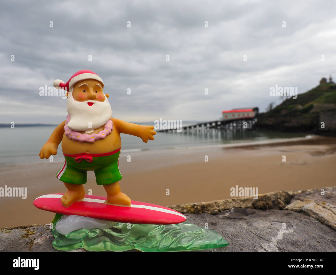 Surfen Santa auf der North Beach in Tenby Pembrokeshire mit der rnli Lifeboat Station im Hintergrund Stockfoto