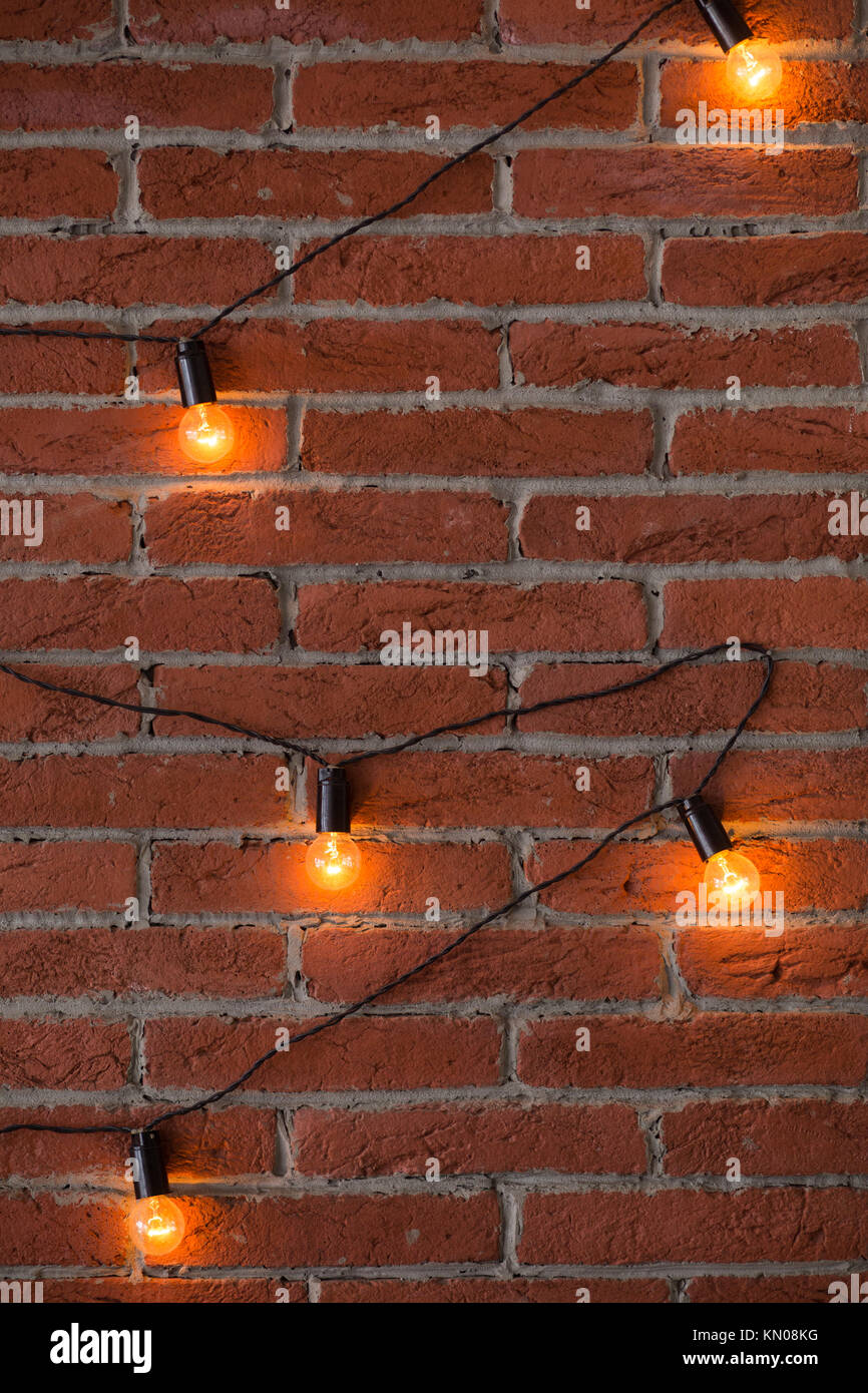Braun Mauer mit leuchtenden orange Anzeigelampe leuchtet. Viele helle Glühbirnen auf schwarzes Kabel. Vertikale Farbfotografie. Stockfoto