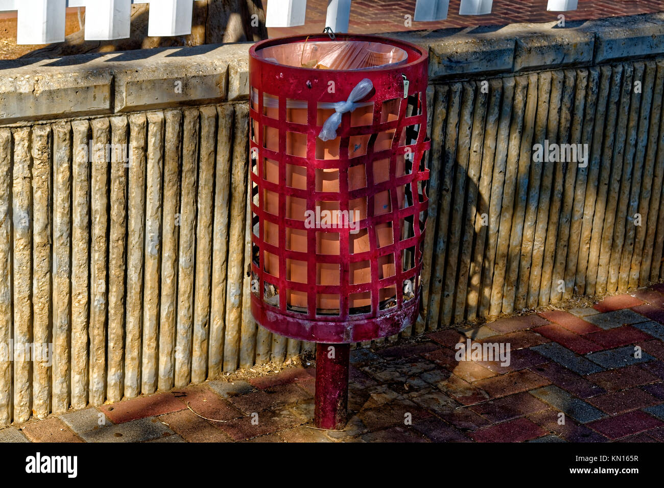 Rusty gekrümmten roten Mülleimer auf der Straße mit einem Zaun Hintergrund und eine Plastiktüte Stockfoto