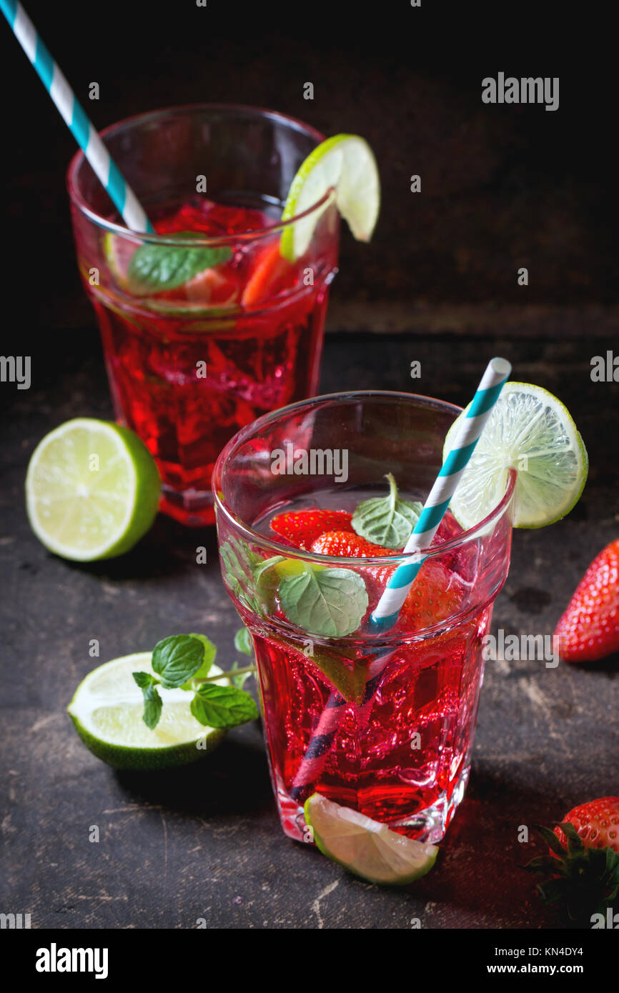 Zwei Gläser mit Retro cocktail Rohre mit hausgemachten Erdbeer Limonade, serviert mit frischen Erdbeeren, Minze, Limette und Eiswürfel overdark Hintergrund. Stockfoto