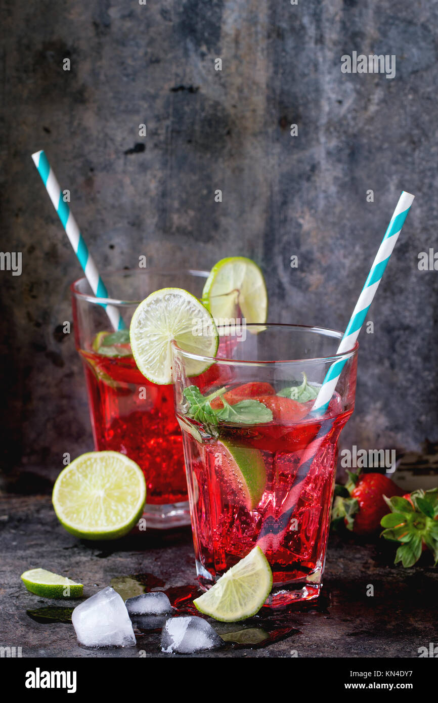 Zwei Gläser mit Retro cocktail Rohre mit hausgemachten Erdbeer Limonade, serviert mit frischen Erdbeeren, Minze, Limette und Eiswürfel overdark Hintergrund. Stockfoto