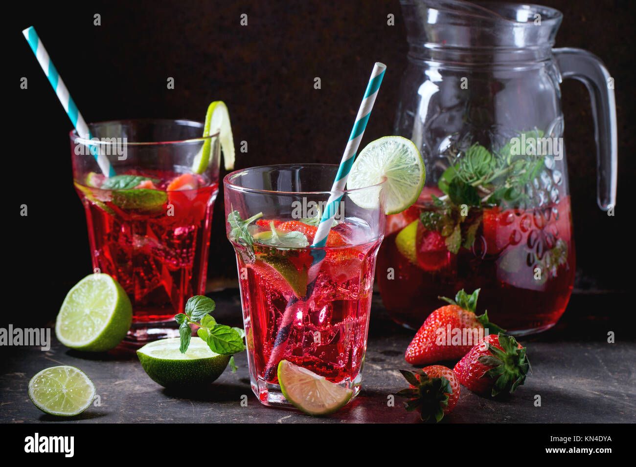 Zwei Gläser mit retro Cocktail Rohre und glaskanne von Erdbeer Limonade, serviert mit frischen Erdbeeren, Minze und Limette über dunklen Hintergrund. Siehe se Stockfoto