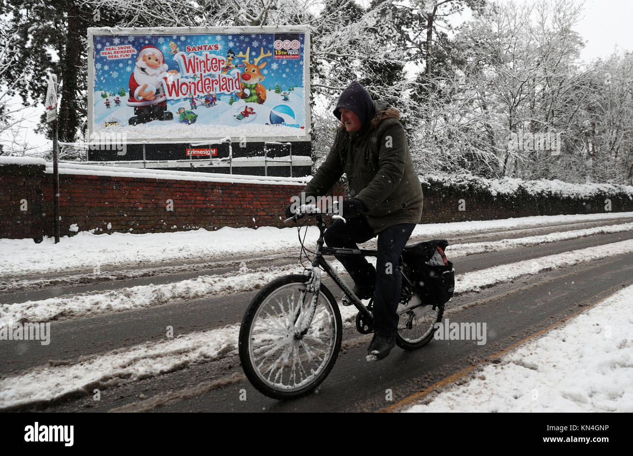 Ein Radfahrer fährt vorbei an einem verschneiten Zeichen Werbung Santa Winterlandschaft in Worcester, wie starker Schneefall über Teile von Großbritannien weitverbreitete Störungen verursacht, schließen Straßen und Erdung Flüge am Flughafen. Stockfoto