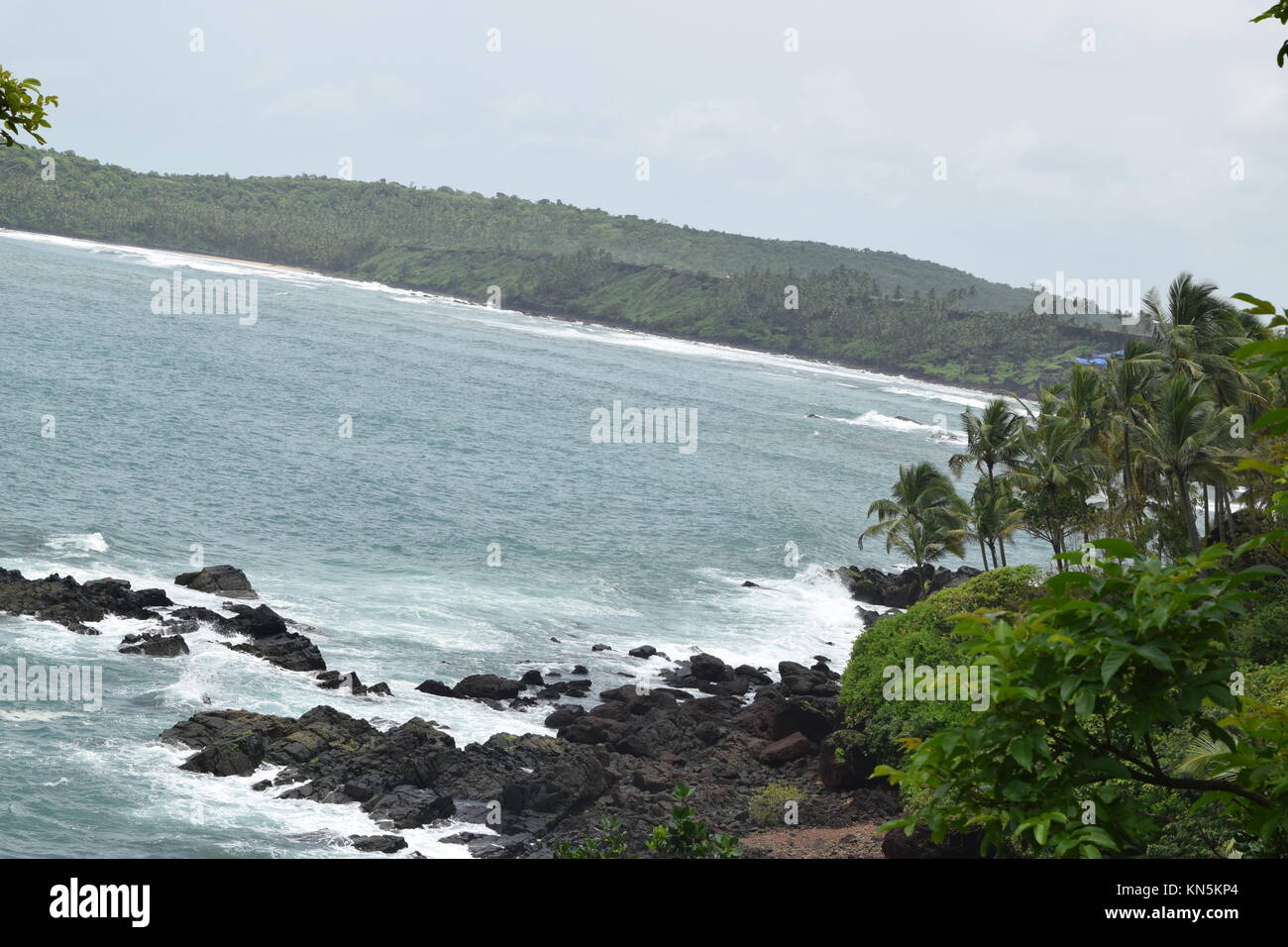 Ausblick auf das Meer und die Berge. Das Meer und die Berge. Rocky mit Meerblick mit Kokospalmen in der Seite. Meer von Grün und Bergen umgeben. Stockfoto