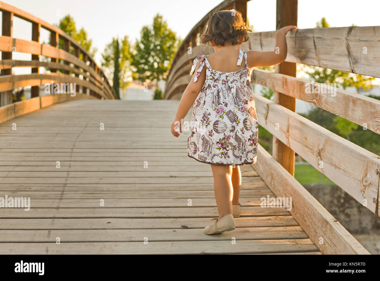 Kleines Mädchen beim Überqueren einer Holzbrücke. Ansicht von hinten. Stockfoto