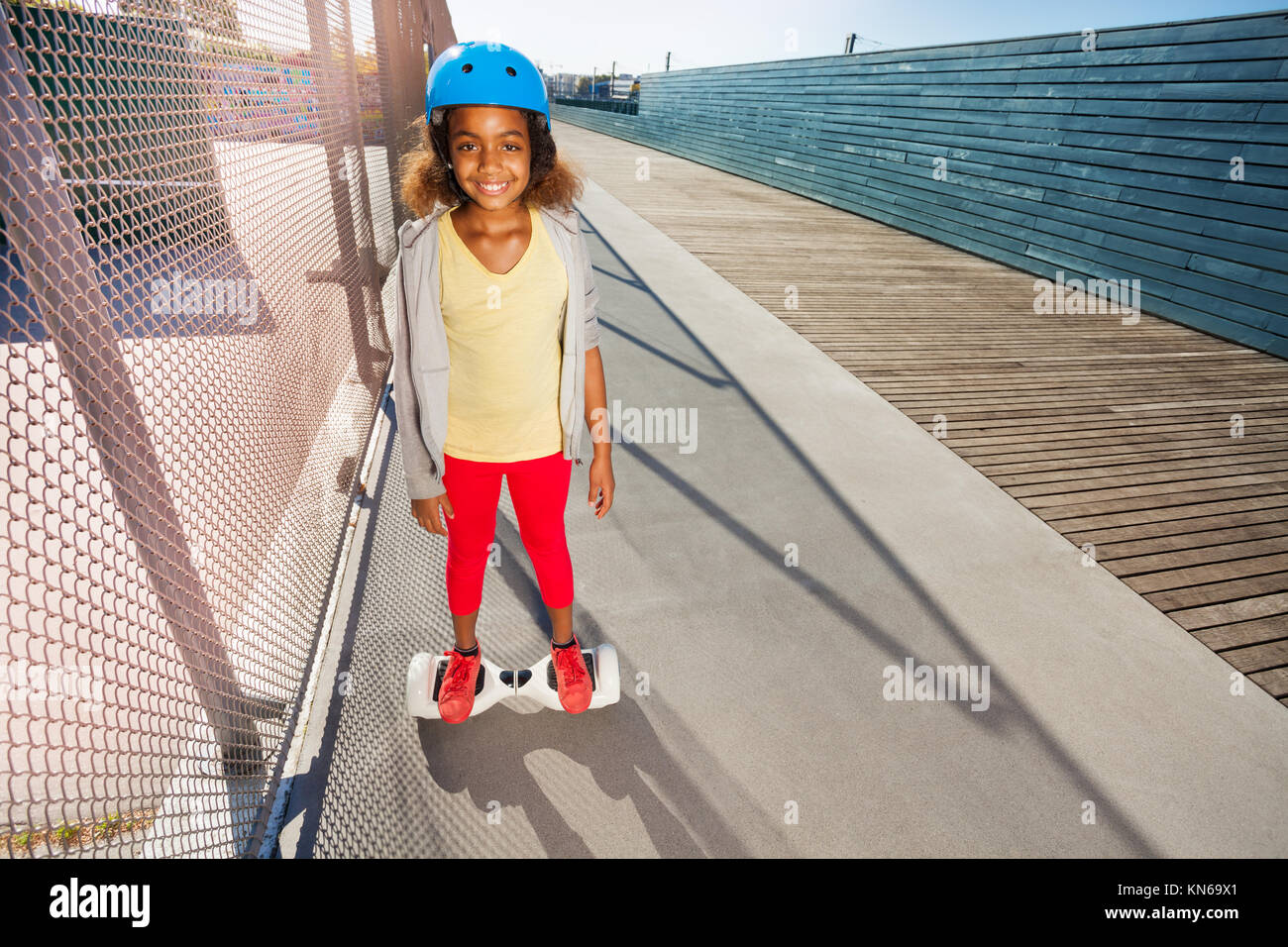Happy afrikanisches Mädchen in Helm reiten Hoverboard auf der Seite Spaziergang an einem sonnigen Tag Stockfoto