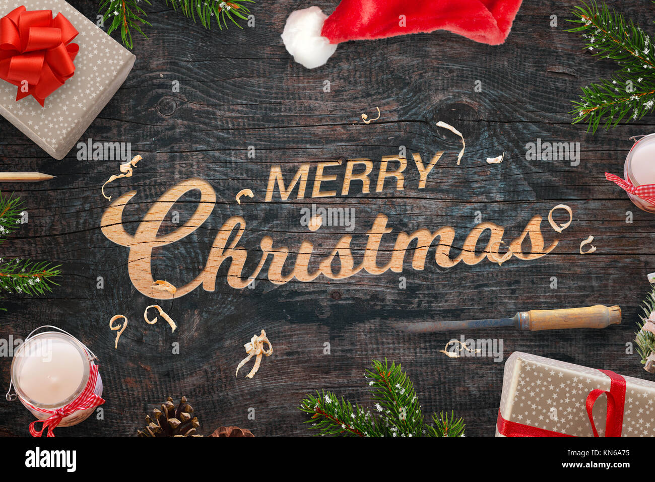 Frohe Weihnachten Gruß in eine Holzoberfläche geschnitzt. Weihnachtsgeschenke, Äste, Meißel, Kerzen, Kiefernzapfen und Santa Claus hat neben. Stockfoto