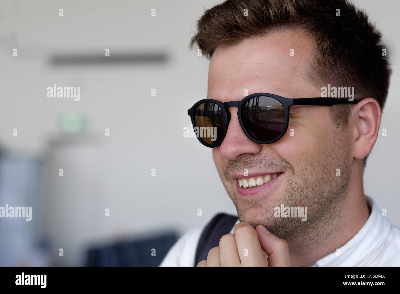 Ein lächelnder Mann in Sonnenbrille schaut aus dem Fenster auf dem Flughafen Stockfoto