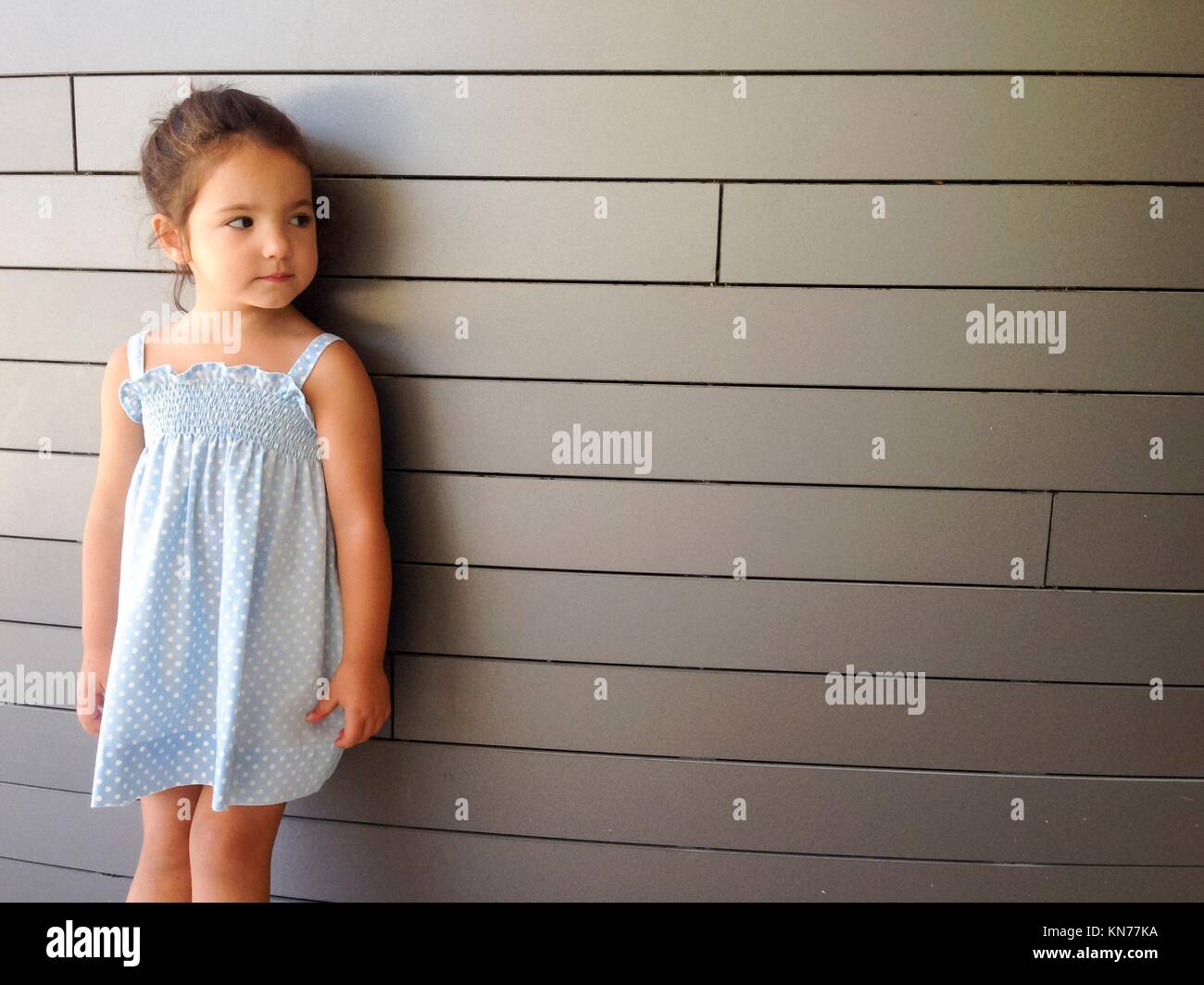 Hübsches kleines Mädchen stehend über moderne Mauer mit Sommerkleid. Stockfoto