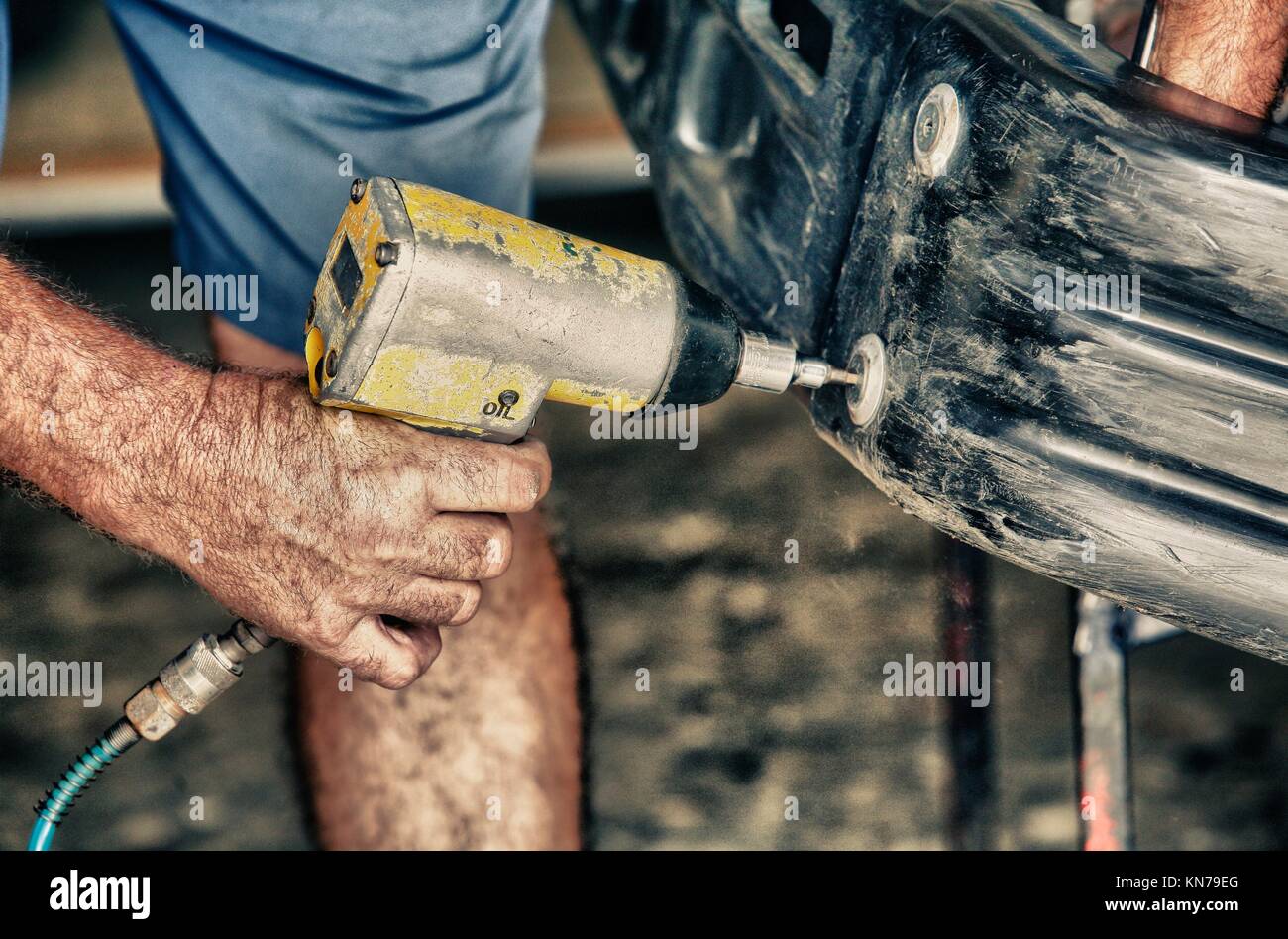 Automechaniker herein- oder herausdrehen vom Auto Stoßstange mit Öldruck Gewehr. Stockfoto
