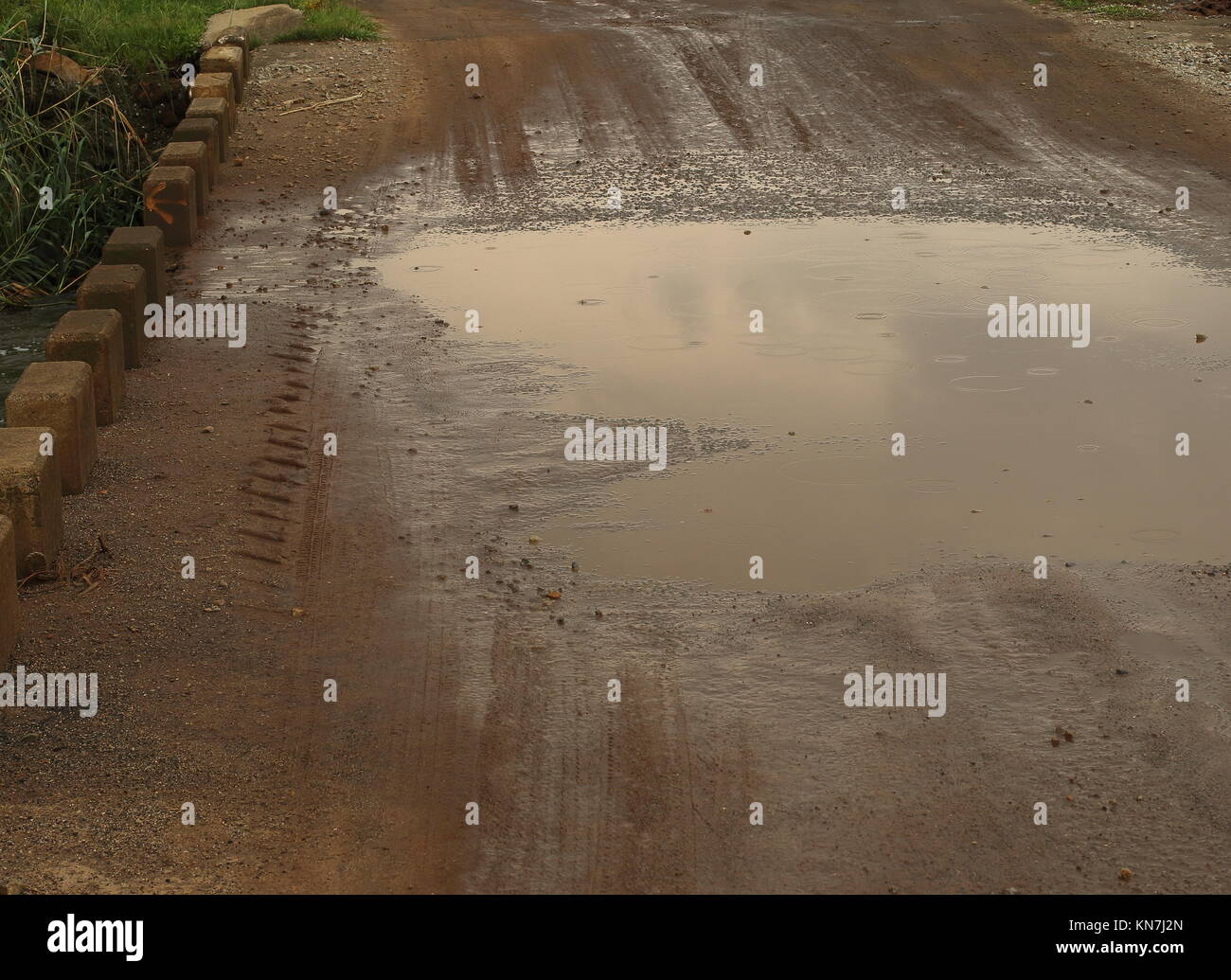 Eine schlammige Pfütze auf einem niedrigen Wasser Brücke auf einem Feldweg an einem regnerischen Tag Bild im Querformat. Stockfoto