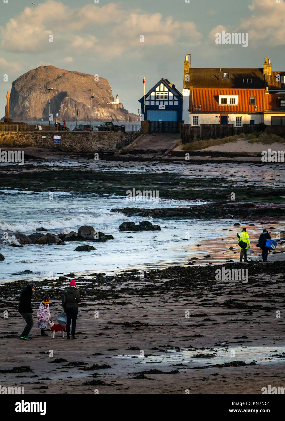 Personen, die im letzten Licht der ein Wintertag am West Bay Beach, North Berwick, East Lothian, Schottland, Großbritannien, und Bass Rock beleuchtet durch die niedrige Sonne Stockfoto