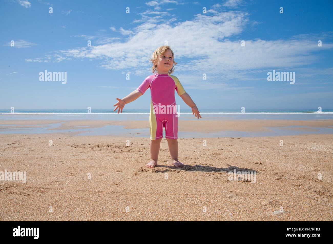 Zwei Jahre alt blond Baby mit rosa und gelb Badeanzug am goldenen Sandstrand am Meer mit 