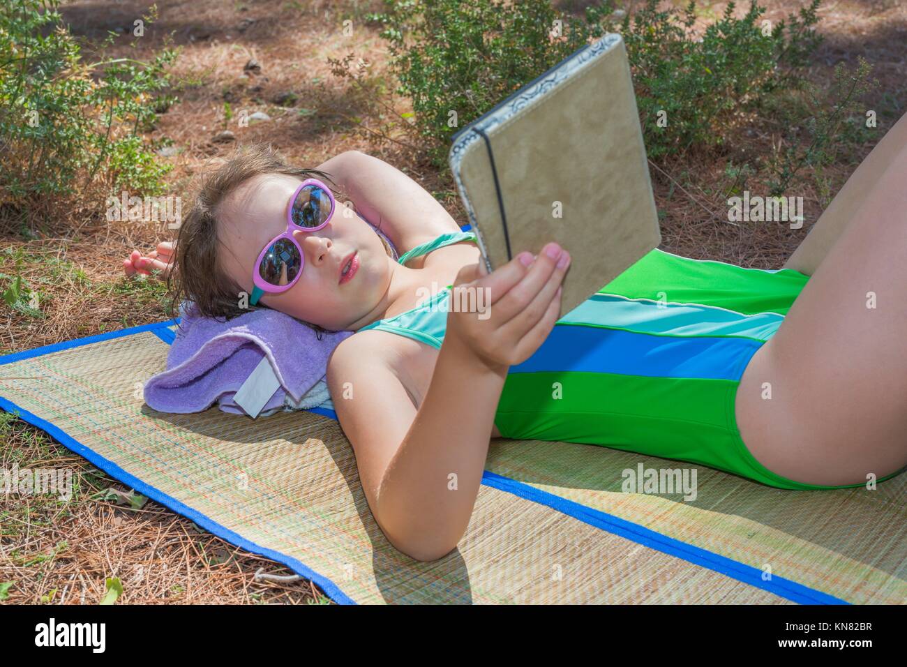 Kleines Mädchen liegen auf dem Plaid mit e-Buch. Stockfoto
