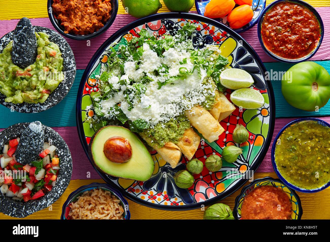 Grüne Enchilada mexikanisches Essen mit Guacamole und Saucen auf bunten Tisch. Stockfoto