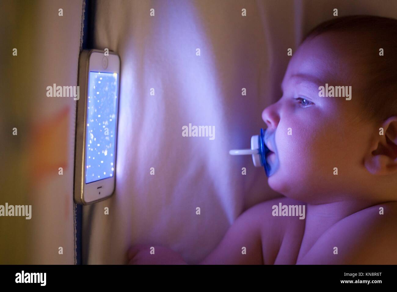 12 Monate altes Baby aufpassen ein Schlaflied cartoons mit Mobiltelefon auf die Krippe. Stockfoto