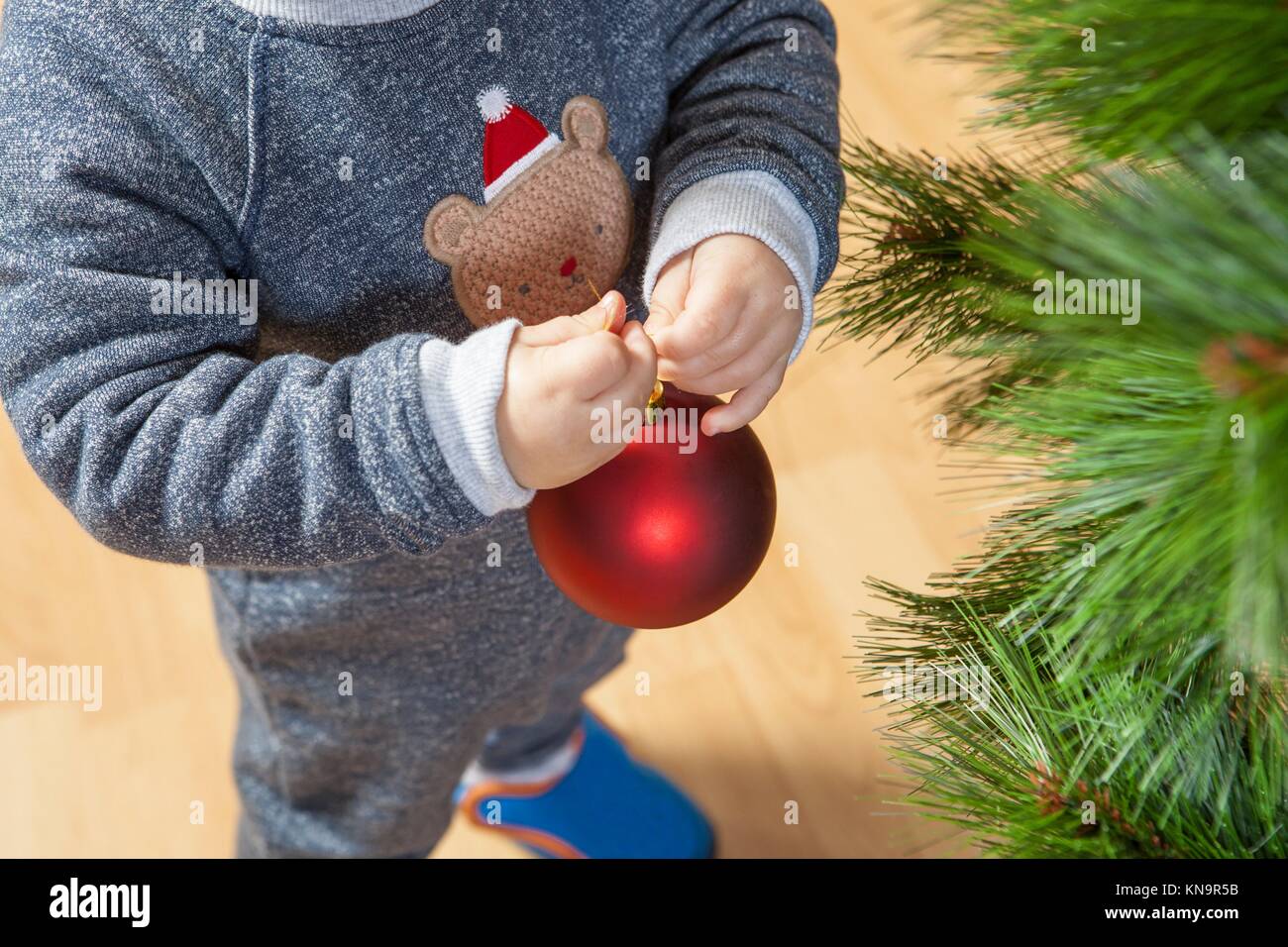 Little baby boy schmückt Weihnachtsbaum mit roten Ball. Stockfoto