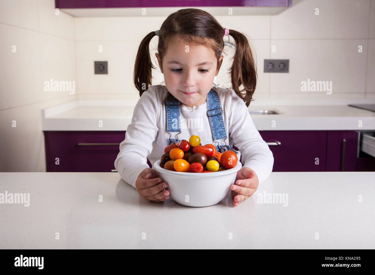 Kleines Mädchen auf der Suche nach einem kirschtomaten Schüssel. Aufklärung über gesunde Ernährung für Kinder. Stockfoto