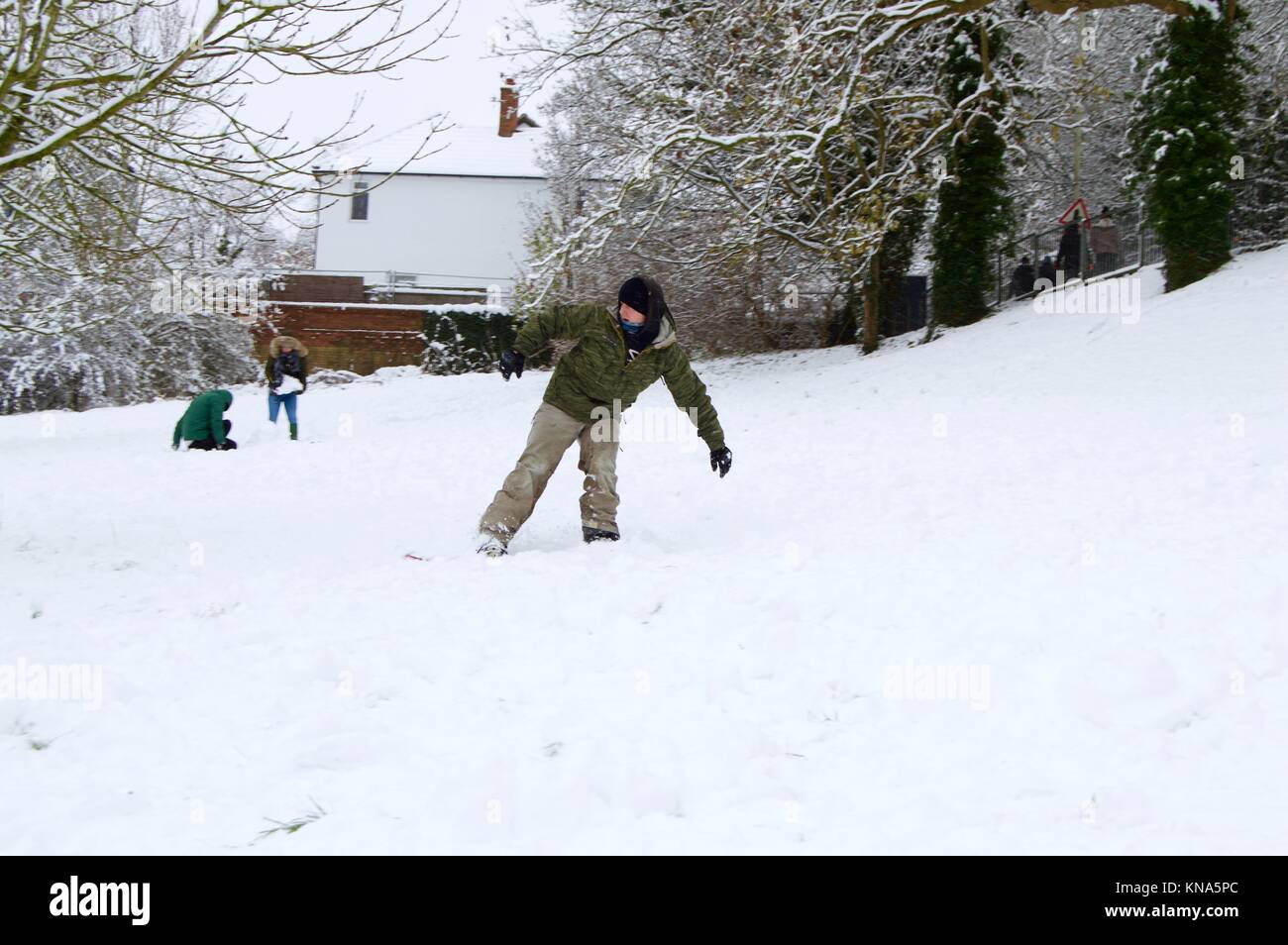 Kinder und Erwachsene genießen die Unerwartete starker Schneefall, Snowboarden und Rodeln den Hügel hinunter in Scharf, Felder, Hemel Hempstead, Hertfordshire Stockfoto