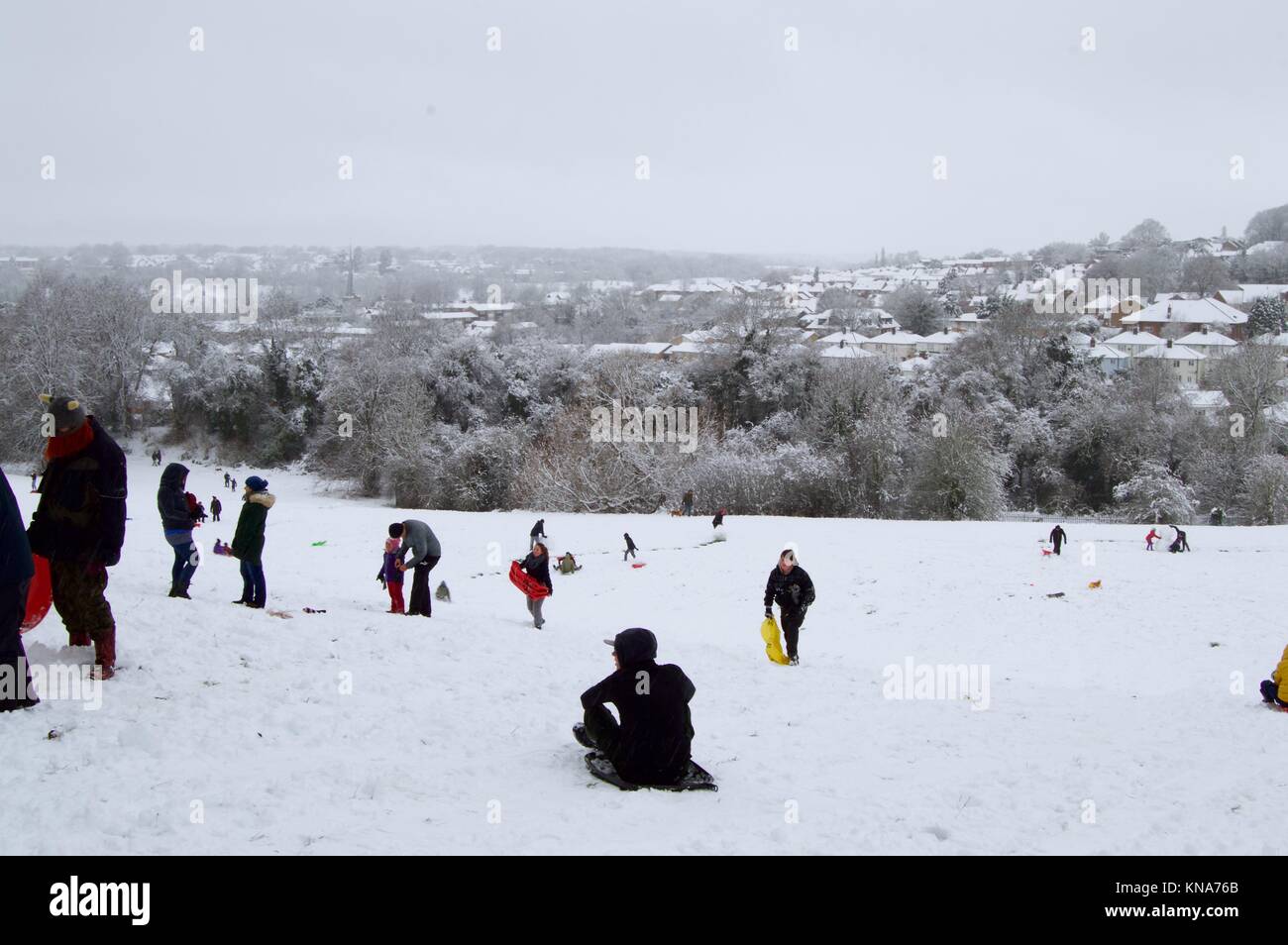 Kinder und Erwachsene genießen die Unerwartete starker Schneefall, Snowboarden und Rodeln den Hügel hinunter in Scharf, Felder, Hemel Hempstead, Hertfordshire Stockfoto