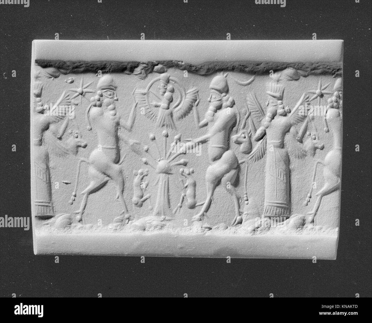 Dieses Zylindersiegel zeigt Stiermänner, die eine Gottheit mit einem heiligen Baum und einer geflügelten Gottheit mit gehörnten Tieren flankieren und antike mythologische Themen illustrieren. Stockfoto